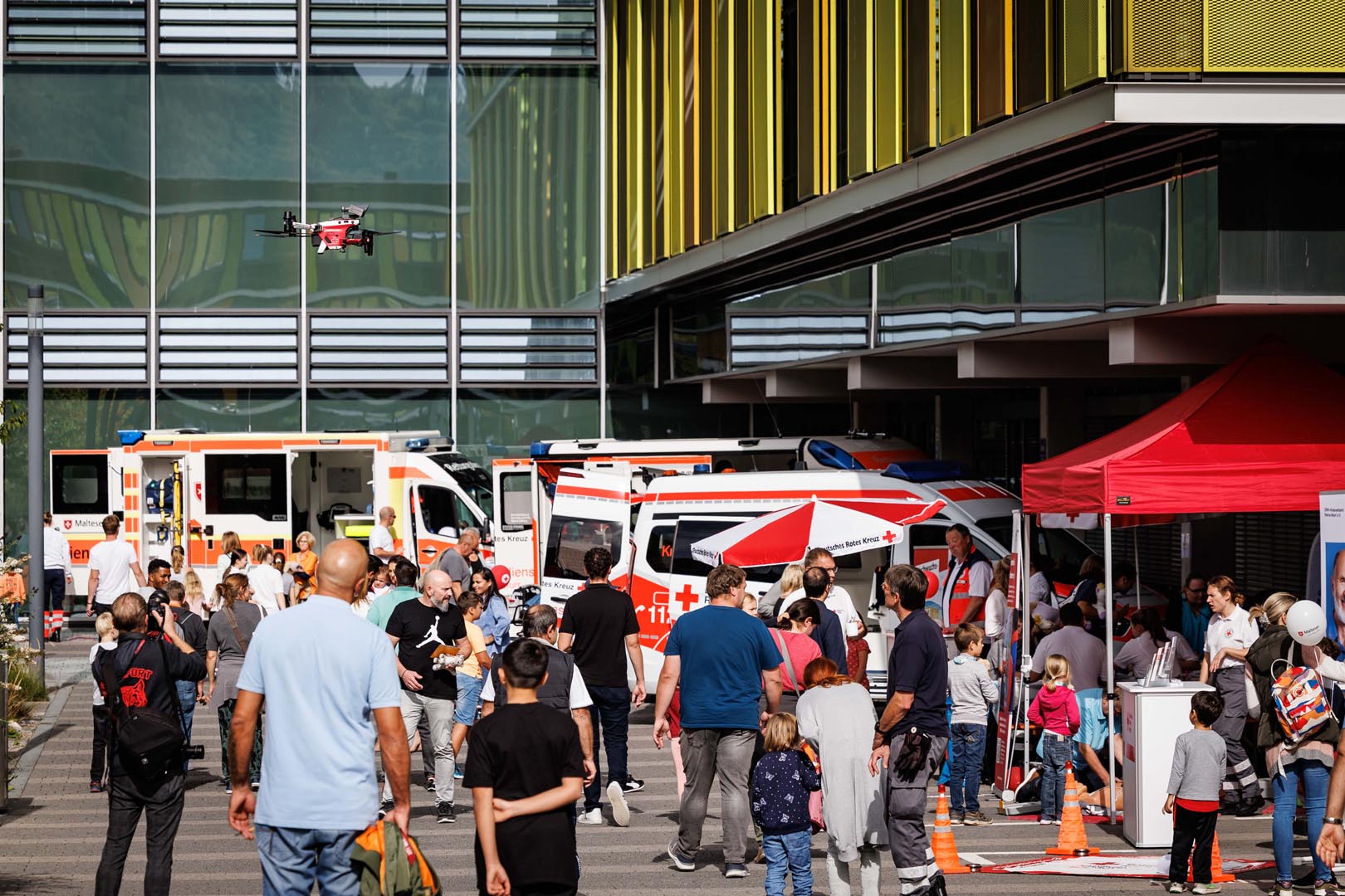 Besucher sehen sich die Einsatzfahrzeuge und eine fliegende Drohne vor dem Klinikum in Winnenden an.