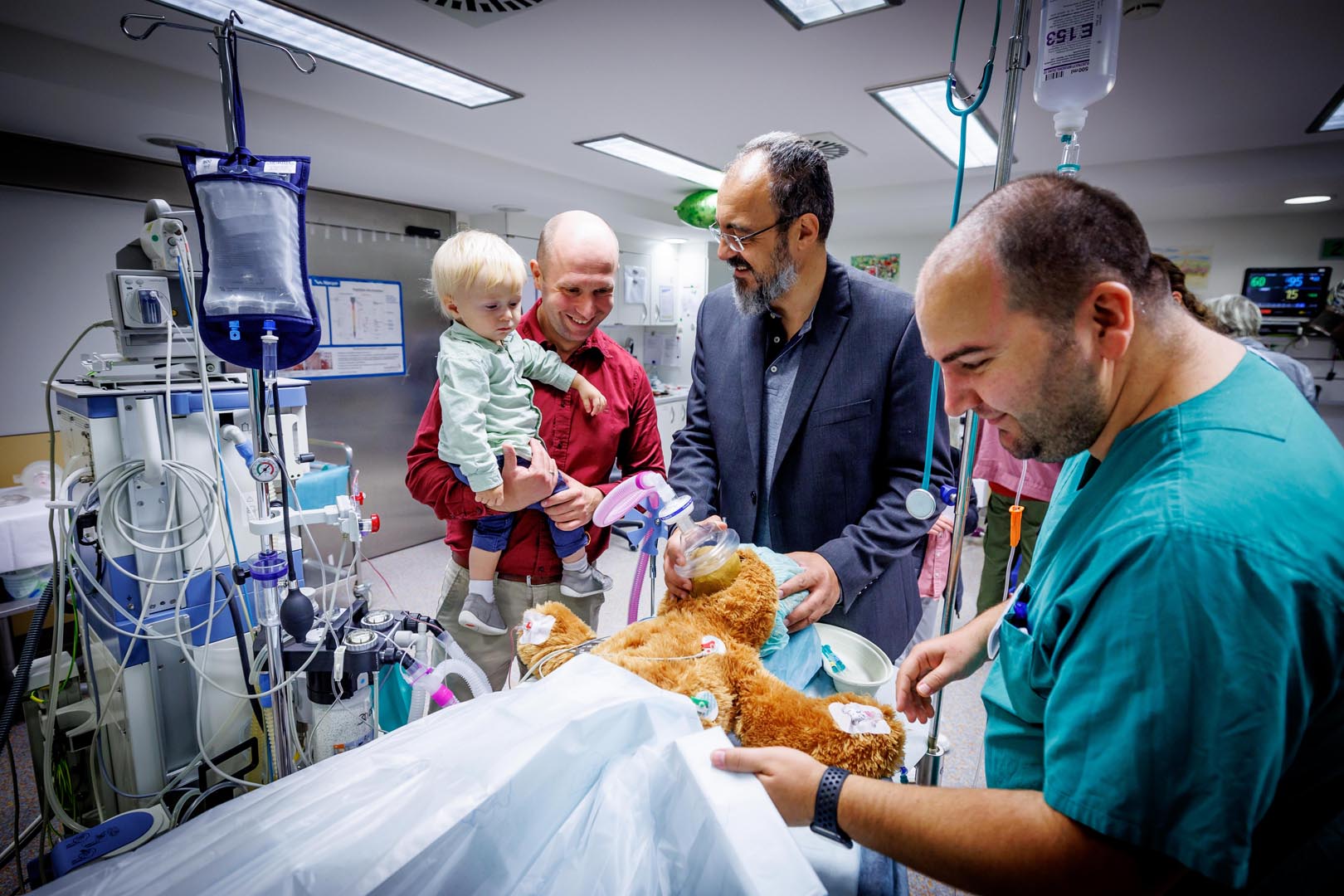 Anästhesie-Chefarzt Dr. Fotios Kefalianakis demonstriert einem Vater mit Kind anhand eines Teddys, wie eine Narkose funktioniert